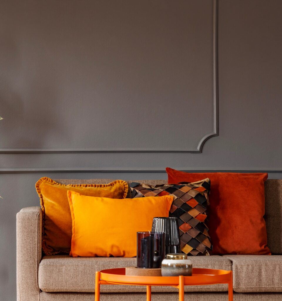 Ficus next to brown sofa with orange pillows in grey living room interior with table. Real photo